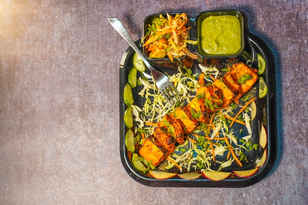 Foto paneer tikka è un piatto indiano a base di pezzi di paneer con salsa e verdure sul tavolo