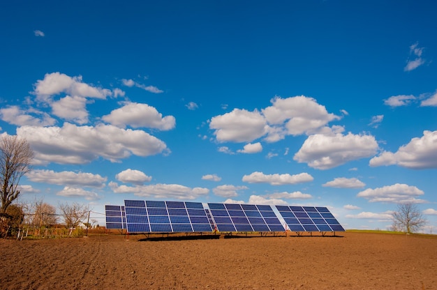 Panel system of solar energy, near the plowed soil of the spring field and beautiful clouds