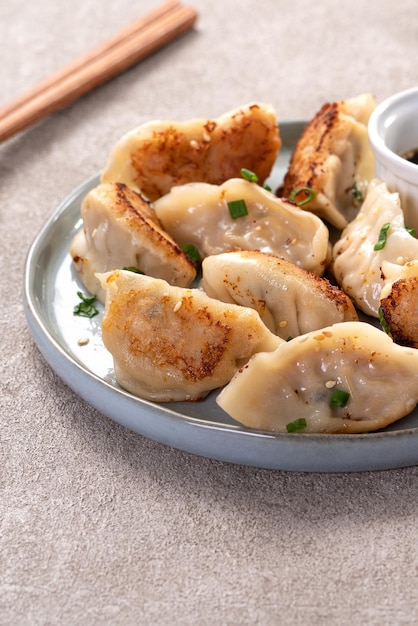 Panfried gyoza dumpling jiaozi in een bord met sojasaus op grijze tafelachtergrond