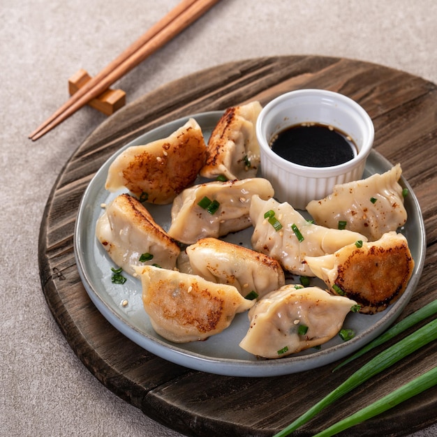 Panfried gyoza dumpling jiaozi in a plate with soy sauce on gray table background