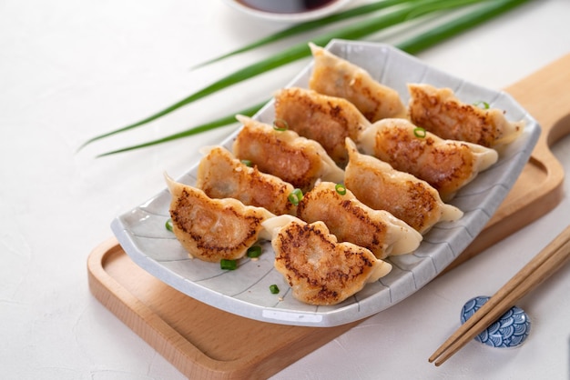 Panfried gyoza dumpling jiaozi in a plate with soy sauce on white table background