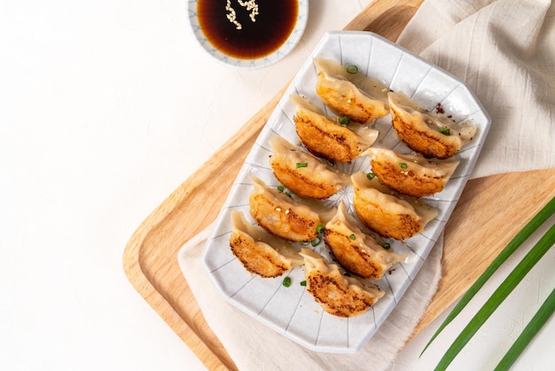 Panfried gyoza dumpling jiaozi in a plate with soy sauce on white table background