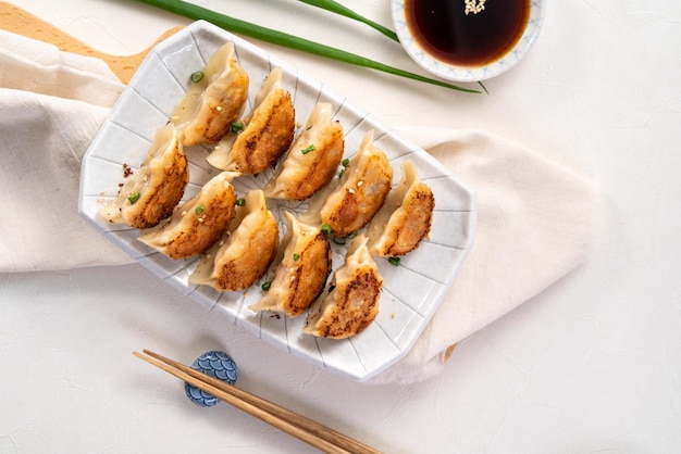 Panfried gyoza dumpling jiaozi in a plate with soy sauce on white table background