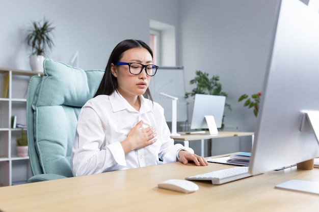 職場でのパニック発作胸呼吸を保持しているオフィスの机に座っている若いアジア女性