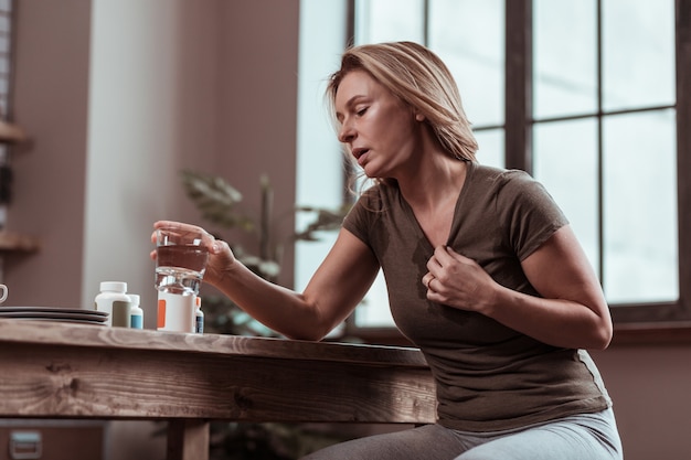 Panic attacks. Blonde-haired mature woman suffering from many panic attacks taking pills and drinking water