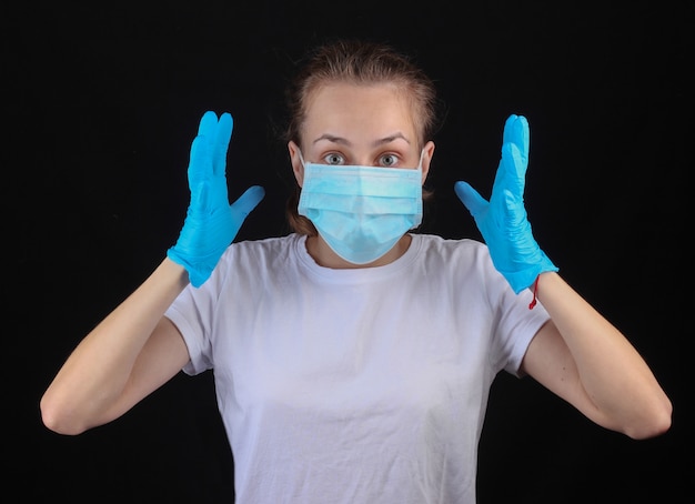 Panic emotional woman in a median face mask, gloves on a black wall.