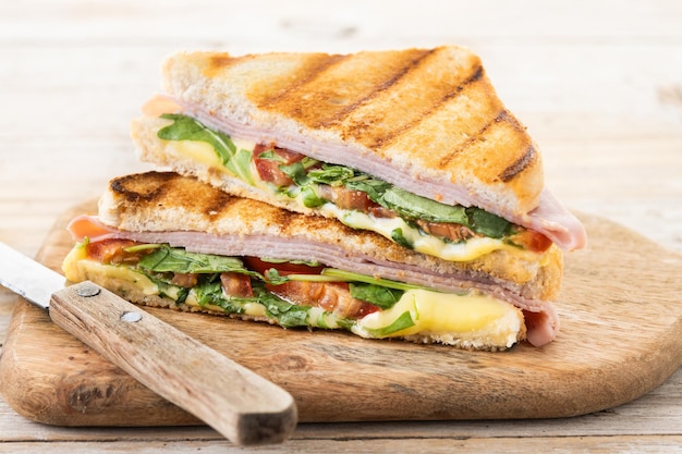 Panini sandwich with ham cheese tomato and arugula on wooden table