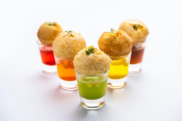 Фото panipuri shot или golgappa shots с водой разных вкусов, подаваемой в маленьких стаканах с индийской закуской из пури с начинкой