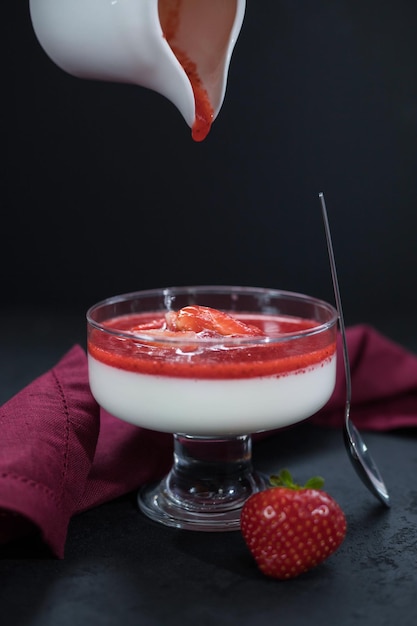 Foto panna cotta met aardbeiensaus en aardbeienbessen in een kom op de zwarte achtergrond