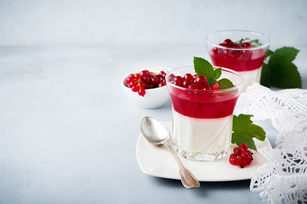 Panna cotta with red currant jelly in vintage glass with leaves of mint and berries on gray stone or concrete.