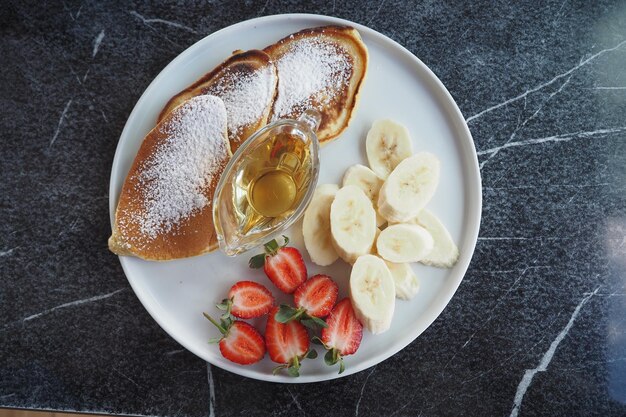 Pannenkoek geserveerd met honing stro bessen en banaan op een bord