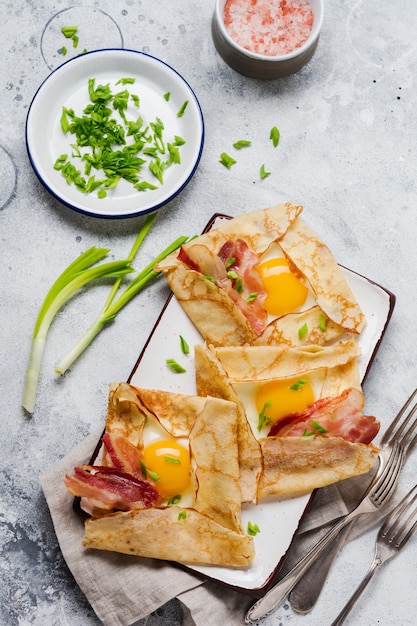 Pannenkoek met gebakken ei, kaas, spek en groene uien als ontbijt op een lichtgrijze betonnen ondergrond