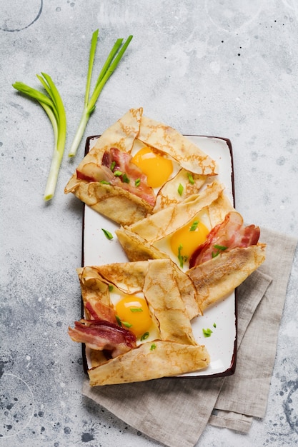 Pannenkoek met gebakken ei, kaas, spek en groene uien als ontbijt op een lichtgrijze betonnen ondergrond