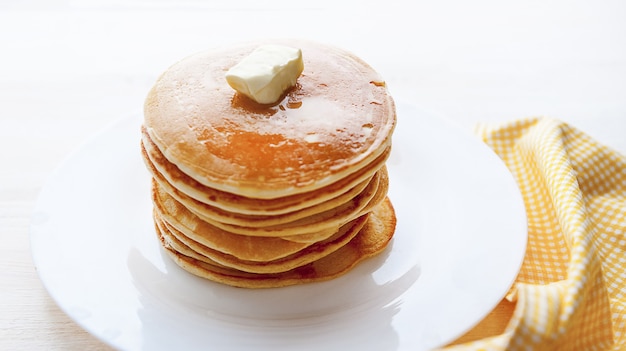 Pannenkoek op een witte plaat met een stuk boter op een houten ondergrond