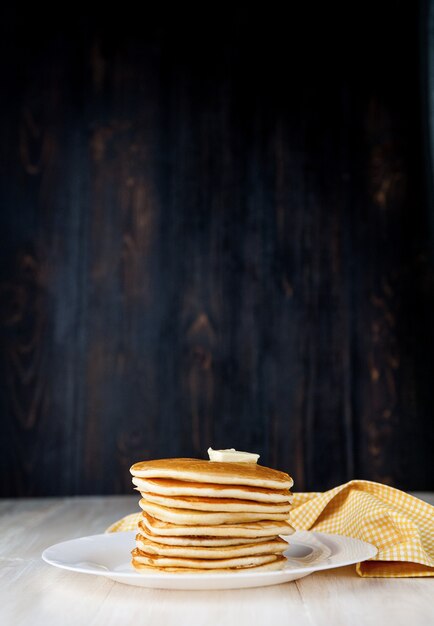 Foto pannenkoek op een witte plaat met een stuk boter op een houten ondergrond