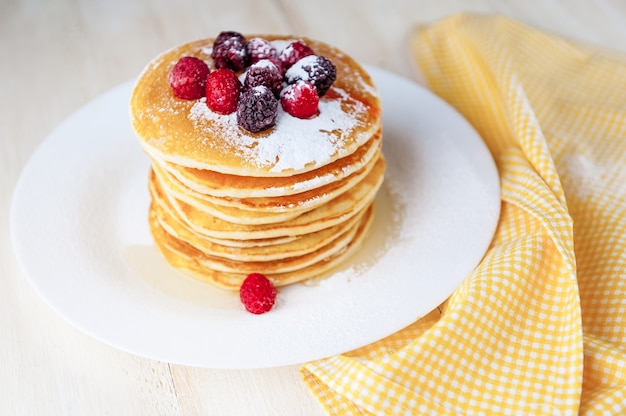 Pannenkoek op een witte plaat met fruit en poedersuiker op een houten ondergrond