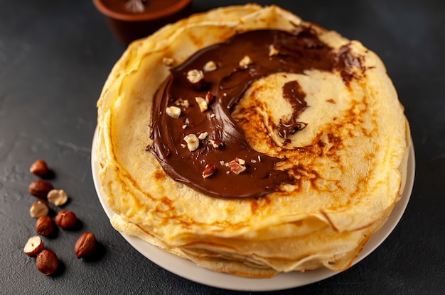 Pannenkoeken met chocolade pasta en hazelnoten, op een witte plaat op een achtergrond van beton, leisteen