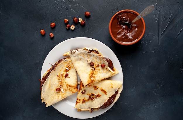 Pannenkoeken met chocolade pasta en hazelnoten, op een witte plaat op een achtergrond van beton, leisteen