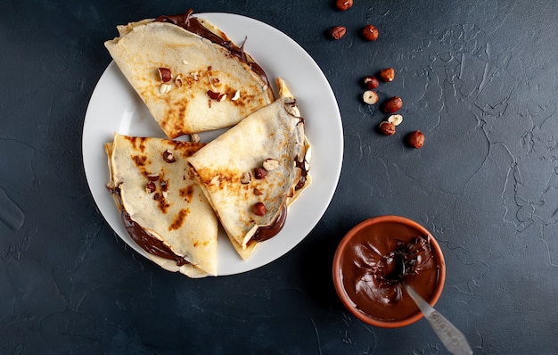 Pannenkoeken met chocolade pasta en hazelnoten, op een witte plaat op een achtergrond van beton, leisteen