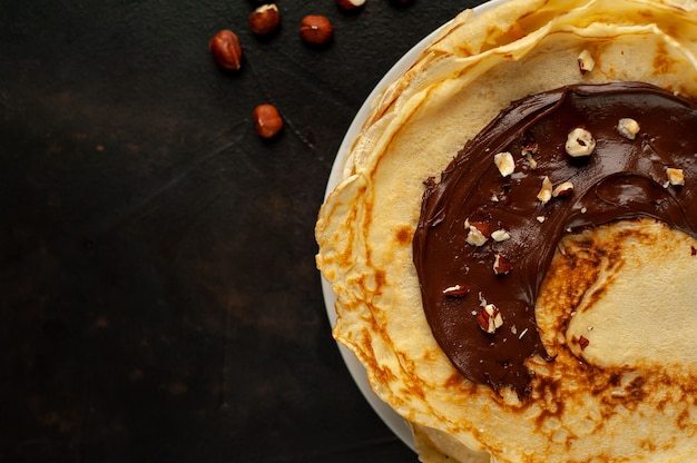 Pannenkoeken met chocoladepasta en hazelnoten, op een witte plaat op een achtergrond van beton, leisteen met kopie ruimte voor uw tekst