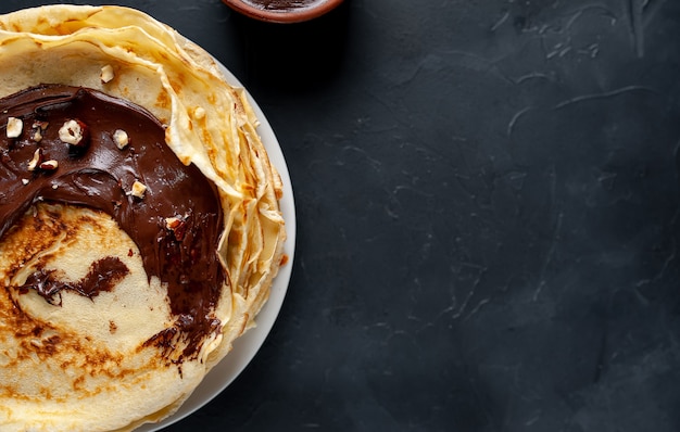 Pannenkoeken met chocoladepasta en hazelnoten, op een witte plaat op een achtergrond van beton, leisteen met kopie ruimte voor uw tekst