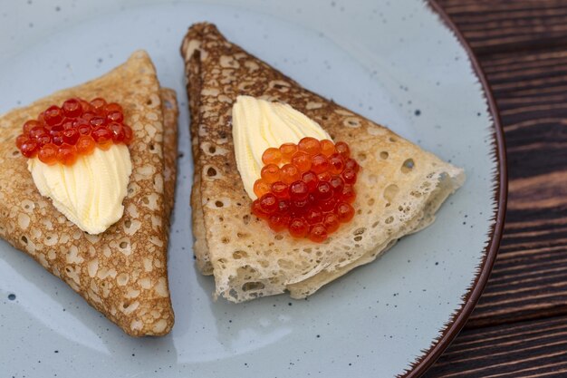 Pannenkoeken met een stuk boter en rode kaviaar op een blauwe plaat Russische tradities carnaval