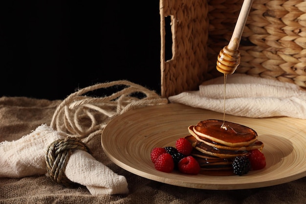 Pannenkoeken met honingframbozen en bramen in een houten plaat op een donkere achtergrond