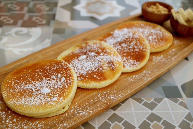 Pannenkoeken met poedersuiker op houten plaat geserveerd op patroon stenen tafel