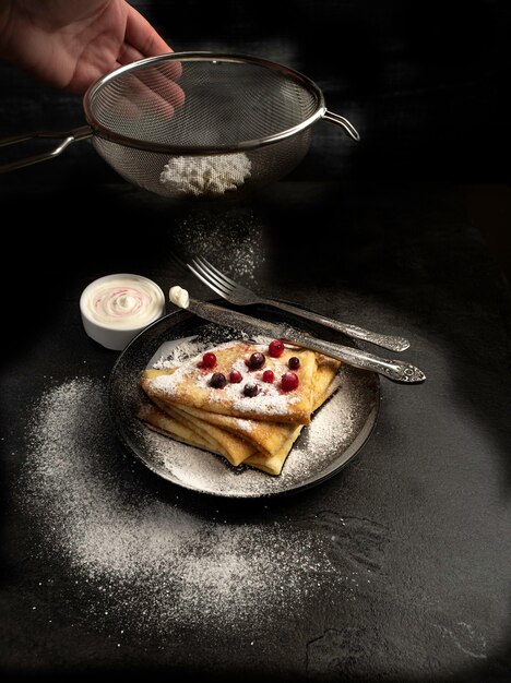 Pannenkoeken met room en bessen en poedersuiker op een zwarte tegel