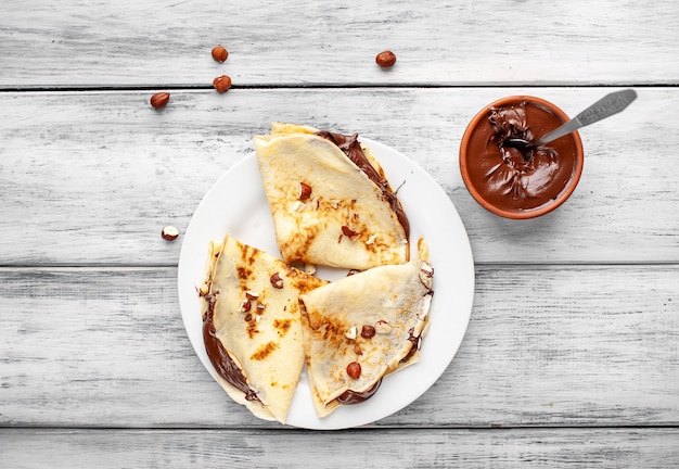 Pannenkoeken met uitgespreide chocolade en hazelnoten, op een witte plaat op een houten achtergrond