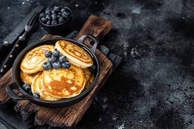 Pannenkoeken met verse bosbessen en ahornsiroop in een pan. Zwarte achtergrond. Bovenaanzicht. Ruimte kopiëren.