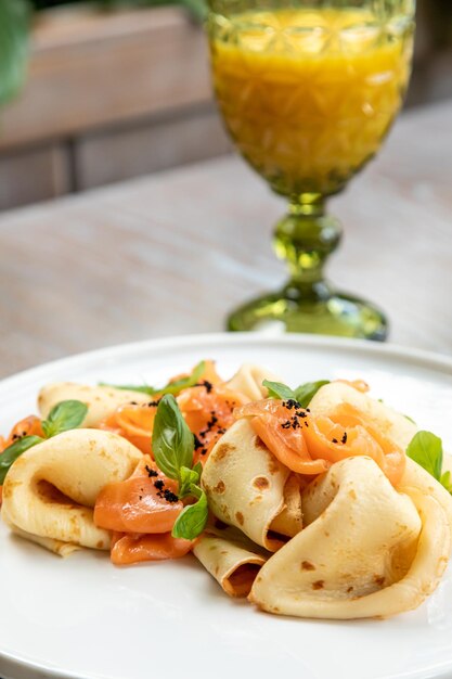 Pannenkoeken met zalm versierd met verse kruiden, geserveerd met sap. ontbijt, foto van het gerecht in het interieur