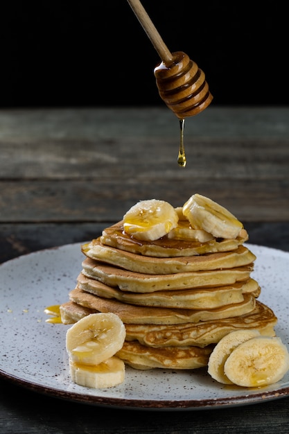 Foto pannenkoeken op de keramische plaat geserveerd met bananen en honing op houten