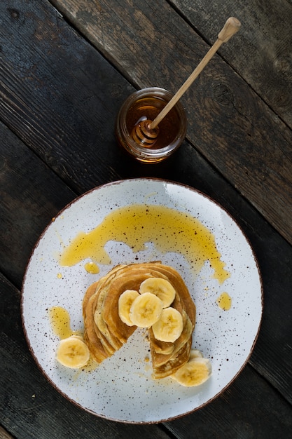 Foto pannenkoeken op de keramische plaat geserveerd met bananen en honing op houten