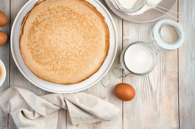 Pannenkoeken op een vlakke witte plaat, ei, suiker en servet op een lichte achtergrond.