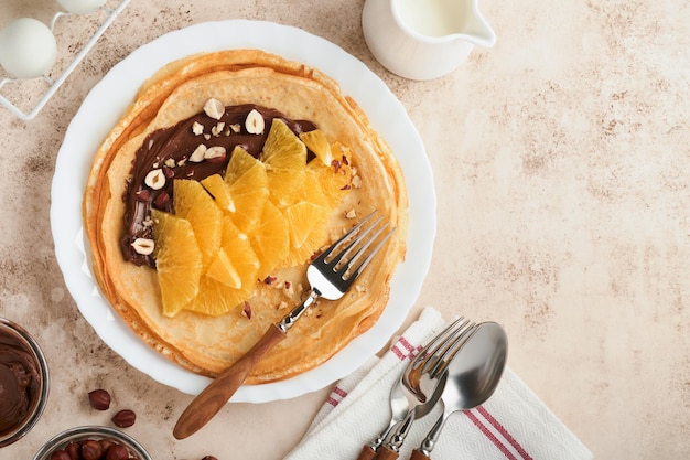 Pannenkoeken suzette met sinaasappelen Dunne pannenkoeken met chocopasta, hazelnoten en sinaasappelschijfjes fruit in witte plaat voor het ontbijt op oude betonnen rustieke tafelachtergrond Kopieer ruimte Bovenaanzicht