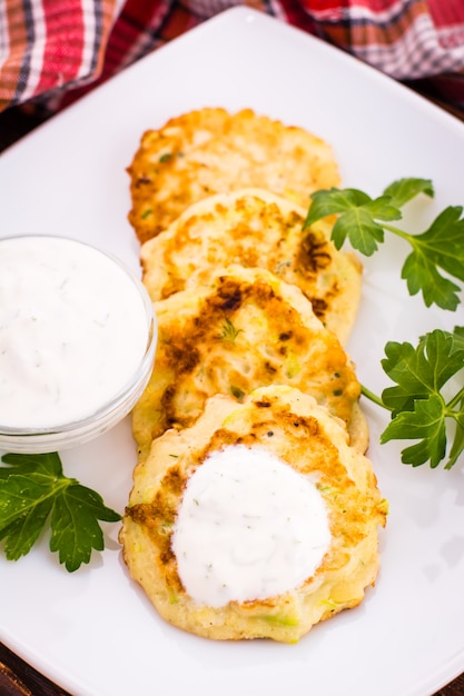 Pannenkoeken van een courgette, saus en peterselie op een witte plaat