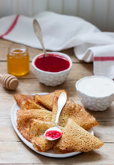 Pannenkoeken van rogge en volkoren geserveerd met zure room, honing en aardbeiensaus. Rustieke stijl.