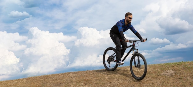 パノラマひげを生やした山の自転車乗りは、美しい空を背景に山に乗る