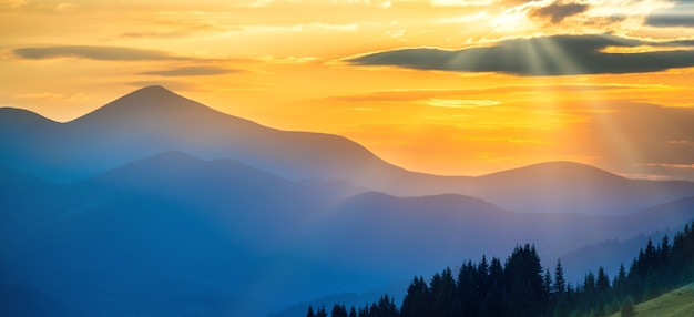 山の美しい劇的な夕日のパノラマ。オレンジ色の雲を通して輝く太陽のある風景