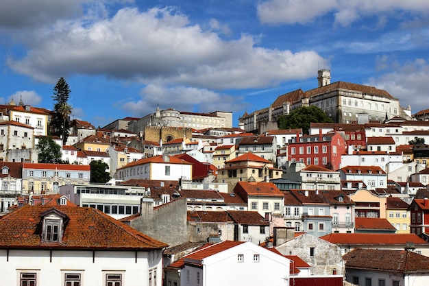 Panorama of Coimbra town former medieval capital of Portugal View of old colorful roofs and houses and university campus with clock tower over blue sky with clouds European travel concept