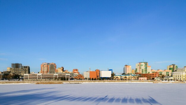 얼어붙은 강과 푸른 하늘 아래 겨울날 햇볕에 쬐인 건물의 파노라마