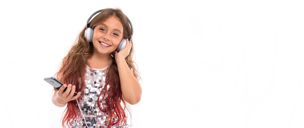 Panorama of girl with big white earphones listening to music, touching her left earphone and holding black smartphone isolated