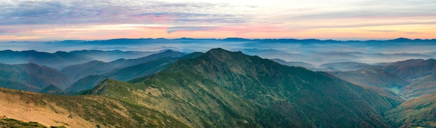 Panorama of green mountains and hills over dramatic sunset sky