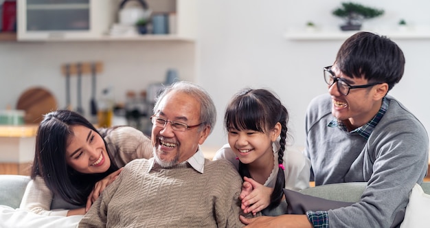 Foto panorama groepsportret van de gelukkige aziatische familie van meerdere generaties zit op de banklaag in de woonkamer met een glimlach.