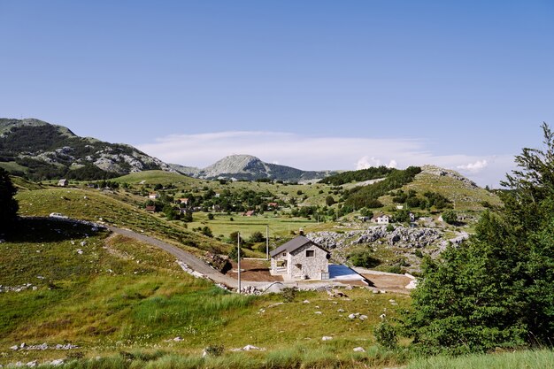 Panorama of a house by the road in a highmountain village among trees grasses and greenery