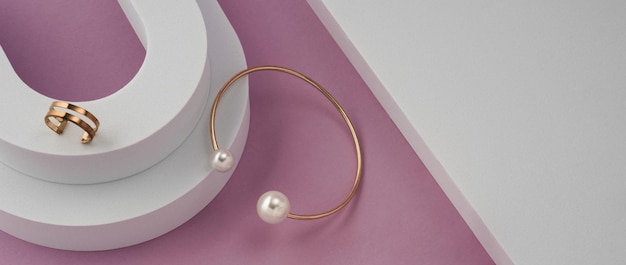 복사 공간이 있는 분홍색 배경의 흰색 연단에 진주 팔찌와 반지가 있는 현대적인 황금의 파노라마