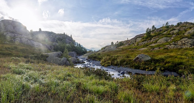 Panorama of mountain scenery in sunny day with meadow located in river valley Caucasus Mountains