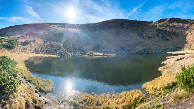 青い水、朝の光と輝く太陽に反射する山の湖のパノラマ
