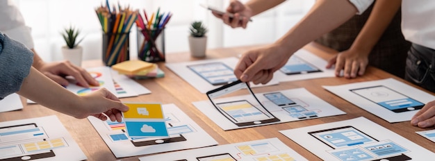 Panorama shot of frontend developer team brainstorming UI and UX designs for mobile app on paper wireframe interface User interface development team planning for userfriendly UI design Scrutinize